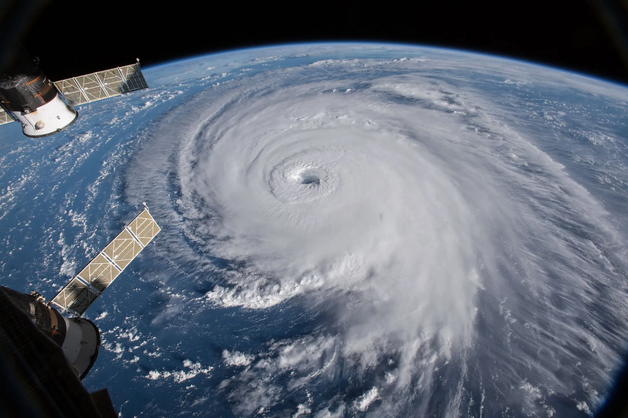 Hurricane Florence seen obliquely from orbit, its eye open at the centre of a broad spiral, with the curve of the Earth's horizon behind it and a solar array of the International Space Station in the foreground.