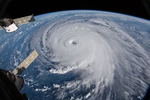 Hurricane Florence seen obliquely from orbit, its eye open at the centre of a broad spiral, with the curve of the Earth's horizon behind it and a solar array of the International Space Station in the foreground.